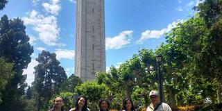 Five individuals stand on a path in front of a bell tower. 