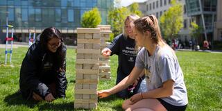 Three students playing Jenga on Gleeson lawn