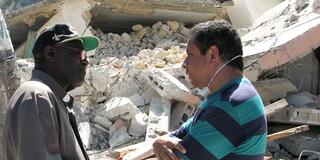 Alfredo Infante, S.J. (left) speaks with Fr. Marat (right), pastor of the destroyed Santa Rosa of Lima’s Church (background) in Leogane, Haiti