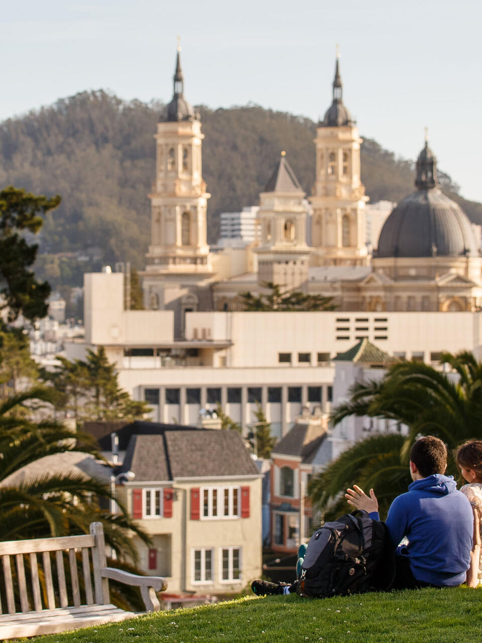 Two students sit on the lawn on a hill overlooking campus